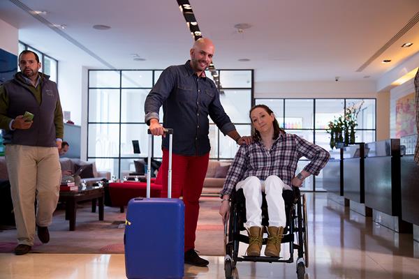 Una mujer en silla de ruedas con su asistente personal posan en la recepción de un hotel