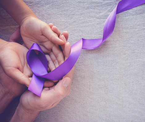 Las manos de dos personas sujetando un lazo morado