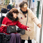 Una mujer en silla de ruedas con su asistente personal en la calle mirando escaparates.