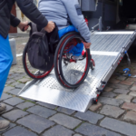 Una persona ayudando a otra en silla de ruedas a subir por la rampa de un vehículo adaptado.