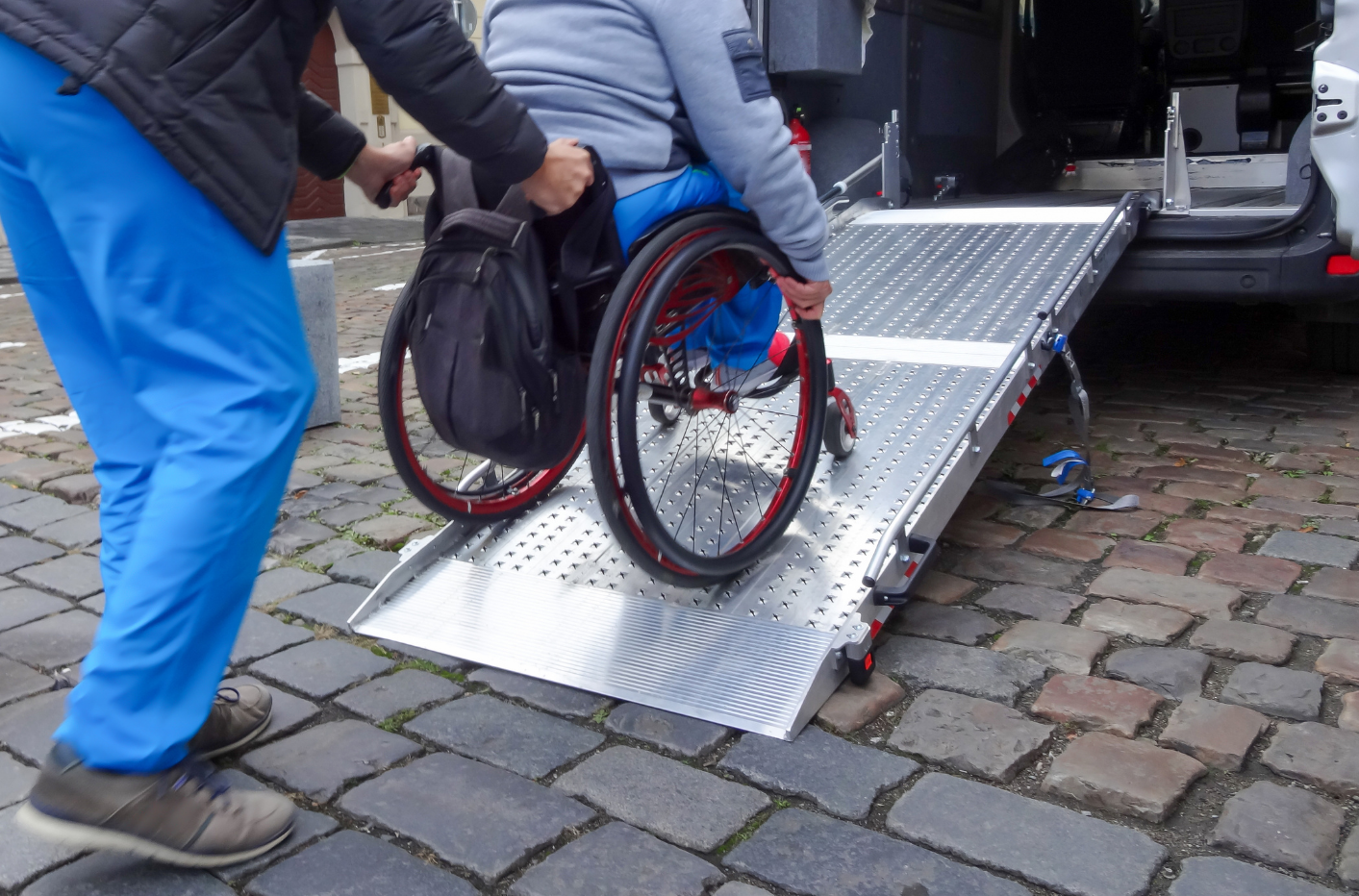 Una persona ayudando a otra en silla de ruedas a subir por la rampa de un vehículo adaptado.